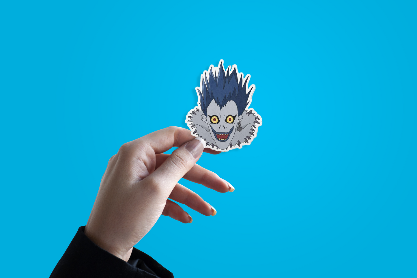 Hand holding a sticker with a death note character's face Ryuk against a blue background