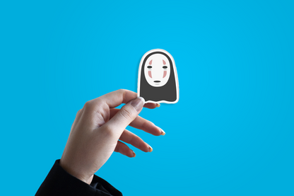 Hand holding a sticker of a character with a black mask against a blue background