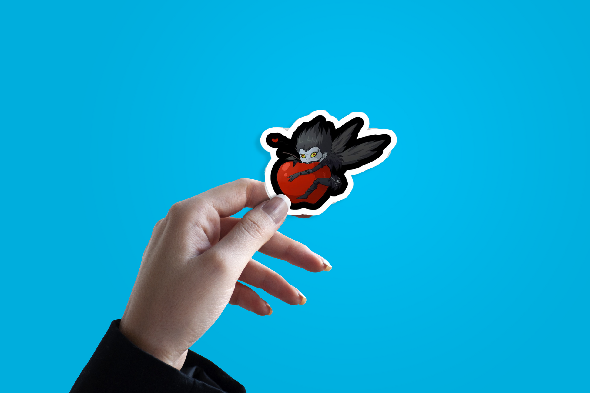 Hand holding a sticker of shinigami/ryuk form Death Note on a blue background.